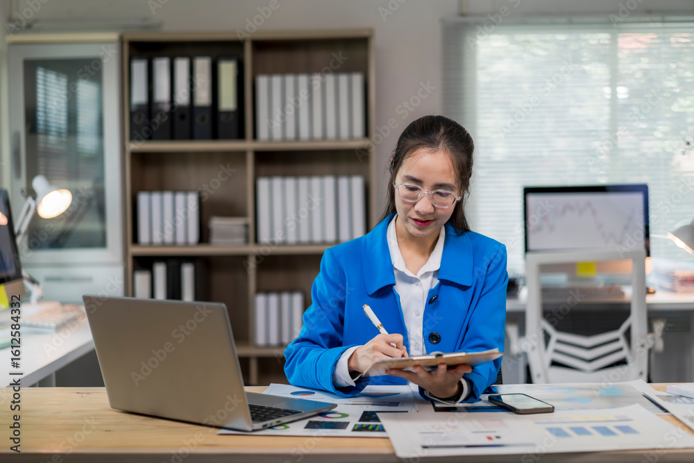 Fototapeta premium woman in a blue jacket is sitting at a desk with a laptop and a notebook