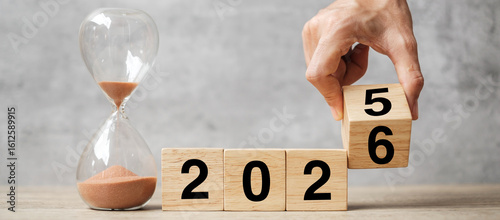 Fotografi hand flipping block 2025 to 2026 text with hourglass on table