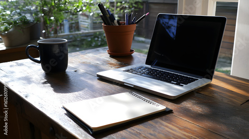 Laptop mug notebook and pen holder on a rustic wooden desk near a window
