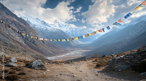 Prayer flags strung across a majestic mountain valley with snow capped peaks and a winding river below