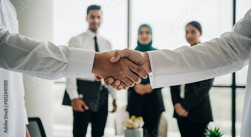 Two businesspeople shake hands in a modern , signifying a successful partnership agreement with colleagues in the background.
