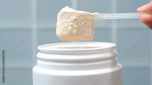 Hand takes protein powder in scoop from plastic jar top view on blue tile background close-up.