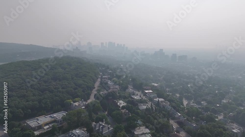 Hazy aerial view of Westmount and downtown Montreal skyline hidden behind smog and trees. c.