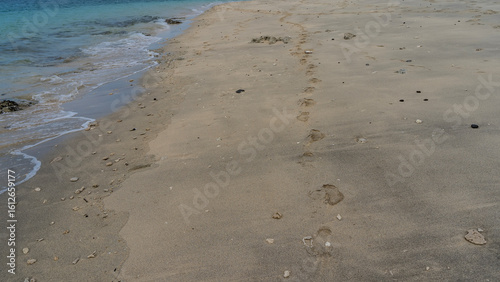 A chain of human bare footprints stretched along the ocean shore. Prints on wet sand. The waves of the turquoise sea are foaming. Madagascar.