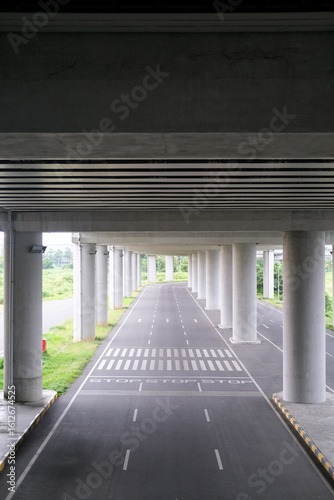 Obraz na plátně Beneath a sprawling overpass, parallel lanes stretch into the horizon, framed by towering concrete pillars and lush greenery, blending urban precision with natural calm in perfect symmetry