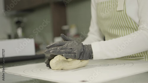 Kneading dough with gloved hands on clean countertop in bright kitchen, showcasing culinary skills and preparation for baking activities.
