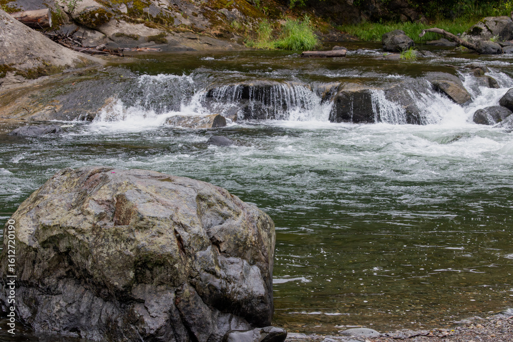 Naklejka premium Green River Waterfalls and Boulder along Filled Forest Bank