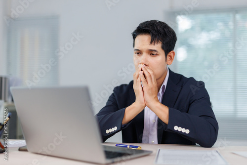 Fototapet Asian businessman covering his mouth with his hands while looking with concern a