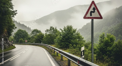 Winding Mountain Road Under a Misty Sky with a Sharp Curve Ahead Warning Sign