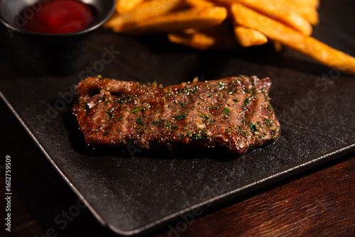 Grilled Beef Steak with French Fries and Ketchup on Black Plate