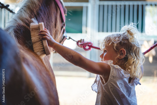 little girl child taking care of her horse, combing and cleaning, show of bonding and affection