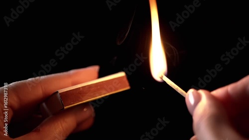 Lighting Match on Matchbox in Dark Room. Female hands lighting and striking match. Burning match, sparks, clouds of thick smoke. Room lighting. Power outage. Slow motion. Close-up.