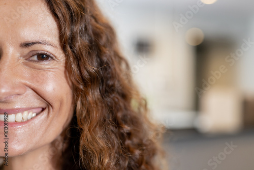 Senior woman smiling with curly hair in lounge with blurred lights and seating, copy space