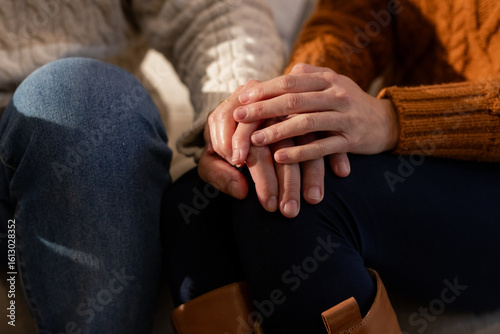 Couple sitting on sofa holding hands gently on lap in living room wearing cable knit sweaters