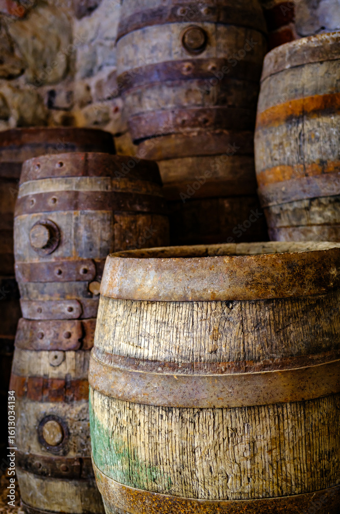 Old wooden barrels stacked against a stone wall in a historic cellar creating an atmosphere of tradition and time-honored craftsmanship Old wooden barrels stacked against a stone wall in a historic cellar creating an atmosphere of tradition and time-honored craftsmanship