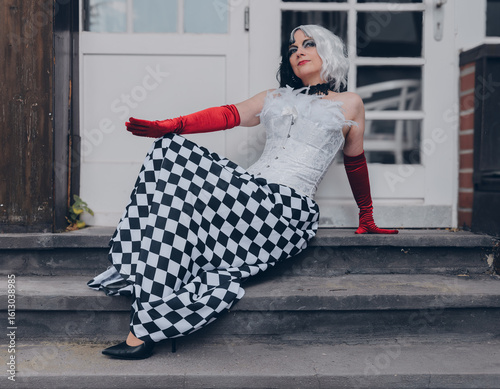 Glamorous figure in checkered attire poses elegantly on steps during a stylish outdoor gathering