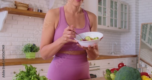 Happy woman eating vegetable salad at home, embracing healthy diet and nourishment, enjoying food in after fitness training or sport workout supports wellness habits through mindful consumption.