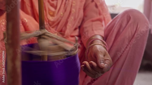 Close-up of a woman’s hand and spinning wheel as she winds purple silk thread, showing traditional Indian textile making at home using handmade tools.