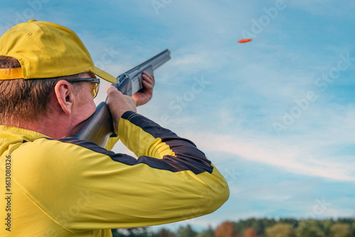 A shooter in a yellow uniform takes a lead before shooting at a clay pigeon