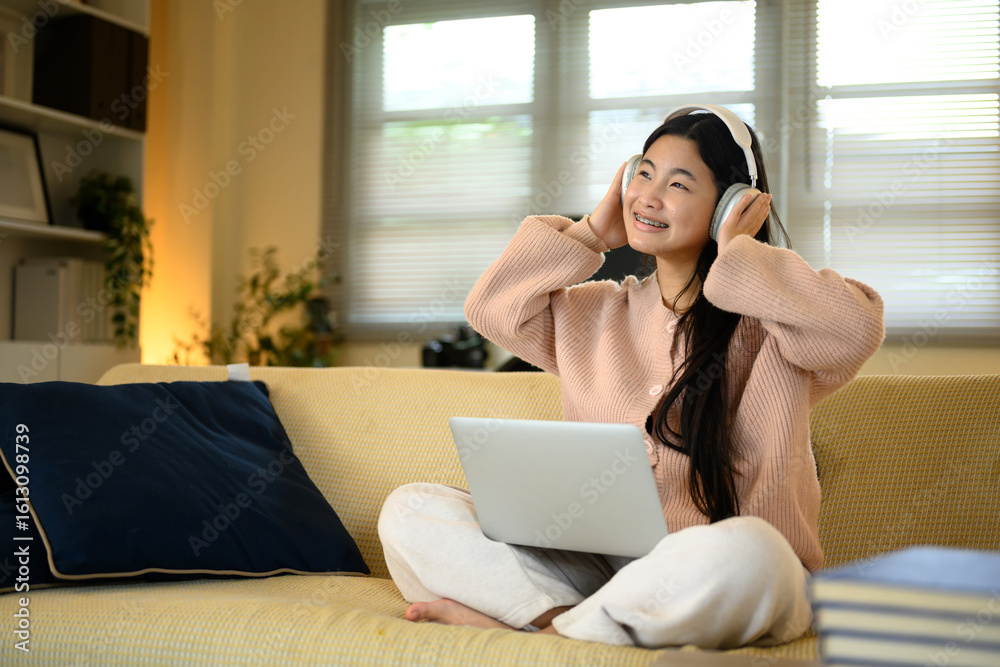 Naklejka premium Cheerful teenage girl enjoying music on headphones with laptop on lap