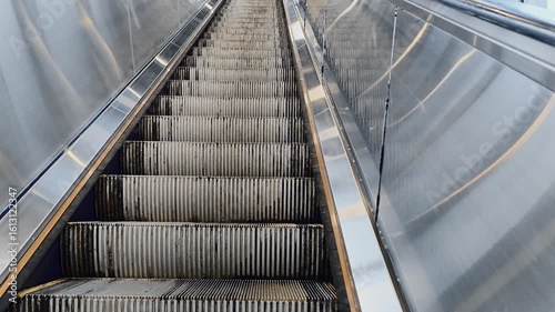 A silver escalator with a few steps missing. The stairs are worn and the escalator is dirty