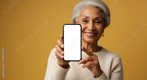 Smiling Senior Woman Holding Smartphone with Blank Screen on Yellow Background