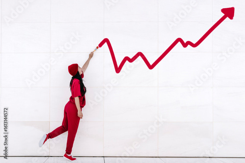 Businesswoman in red pointing at upward graph showing financial growth