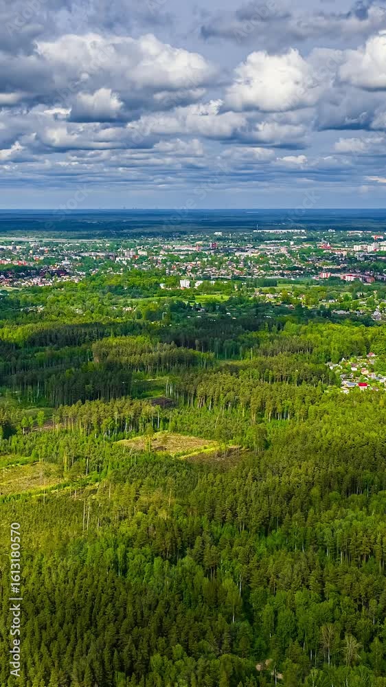 Vertical - aerial timelapse shows clouds moving across the sky above landscape where a vast pine forest meets the scattered buildings of a city in Latvia. Vertical - aerial timelapse shows clouds moving across the sky above landscape where a vast pine forest meets the scattered buildings of a city in Latvia.