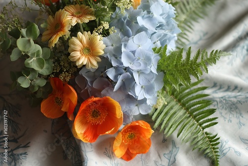 A playful composition of soft blue hydrangeas, pale yellow daisies, and vibrant orange poppies, mixed with fresh green ferns and eucalyptus.