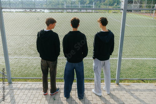 Billede på lærred Three Teen Boys Standing by the Fence at a School Sports Field