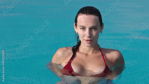 Woman with long dark hair relaxing in a swimming pool, eyes closed, enjoying tranquility and serenity, surrounded by clear blue water, embodying peace and calmness in a sunny environment