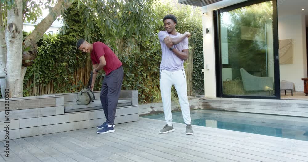 Diverse male friends arriving with duffel sparking shoulder stretching, doing push-ups on pool deck