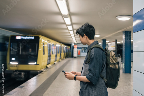 Teenager student girl with backpack waiting for the subway train and using a smartphone on the platform