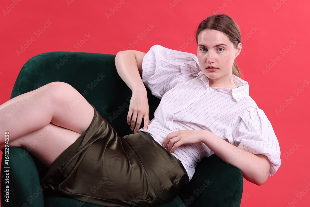 Beautiful young woman sitting on armchair against red background Beautiful young woman sitting on armchair against red background