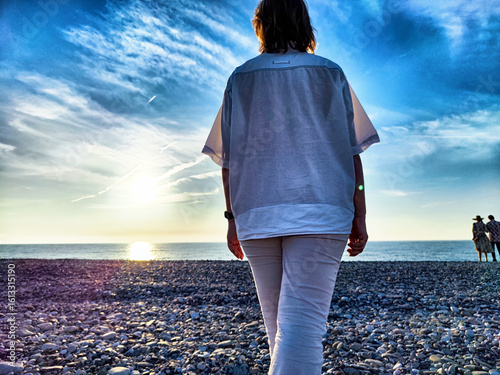 Foto Person walking along a pebbly beach at sunset near the ocean with a tranquil sky