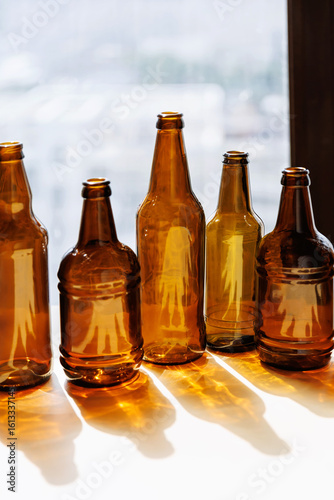 Amber glass bottles lined up by window casting strong golden reflections and deep shadows