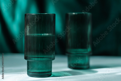 Transparent green glass tumbler with vertical texture casting a soft shadow on a minimalist white surface