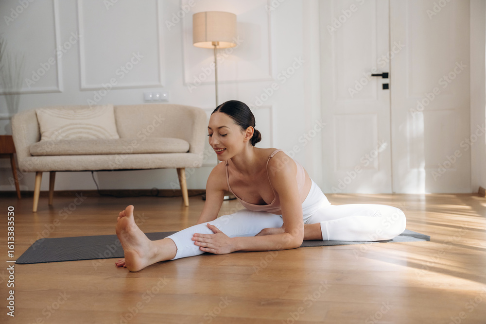 Obraz premium Flexibility exercise for legs. Young woman in fitness clothes is in the room
