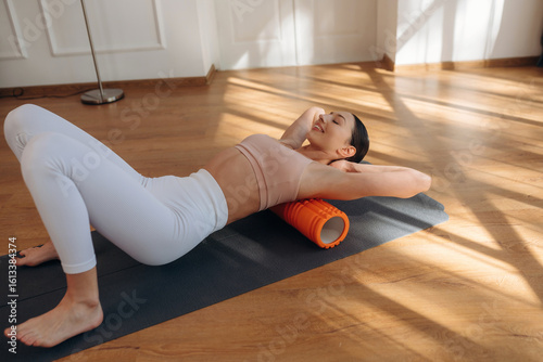 The orange fitness roll. Young woman in fitness clothes is in the room