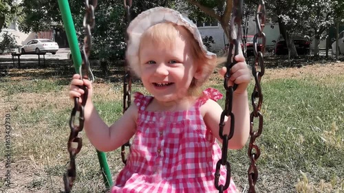 Two-year-old blonde girl riding on a swing and laughing