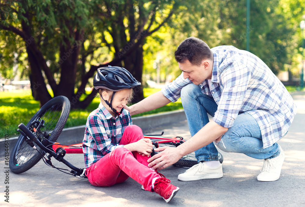 Fototapeta premium Attentive Dad Is Comforting His Daughter After Bike Accident, checking on her leg