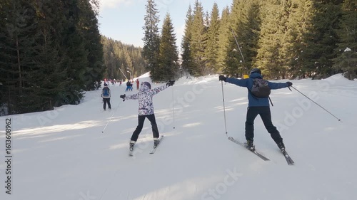 Bansko, Bulgaria - Feb 12, 2025: Two friends skiing together on a snowy mountain slope surrounded by trees spreading hands wide open
