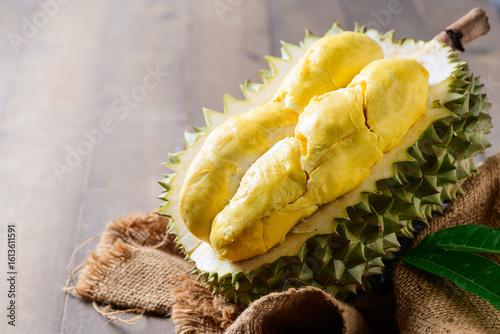 Ripe durian fruit or Durio zibethinus with yellow creamy pulp exposed on wood background. king of fruits