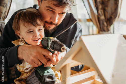 Father assisting son building up birdhouse at home