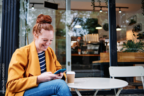 Smiling woman using smart phone while sitting at cafe