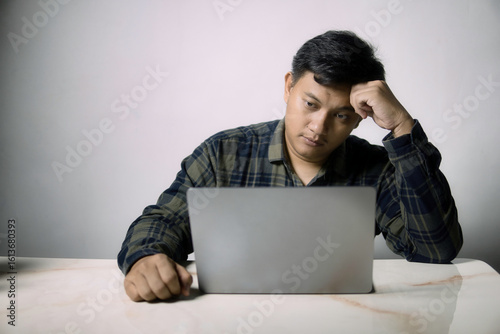 A man looks intently at his laptop, appearing stressed or deep in thought while working or studying. Ideal for themes of remote work, online learning, or digital fatigue.