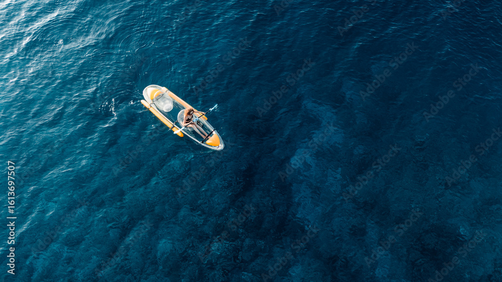Woman swims on transparent plastic kayak in summer blue sea. Drone view, top down Woman swims on transparent plastic kayak in summer blue sea. Drone view, top down