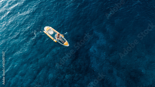 Woman swims on transparent plastic kayak in summer blue sea. Drone view, top down