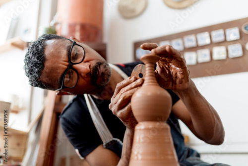 Close-up of male artist making earthenware while sitting in workshop