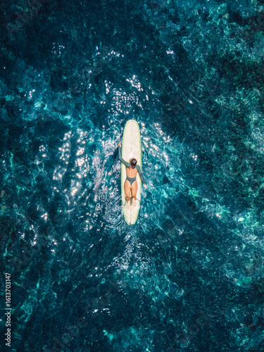 Woman rowing on surfboard in ocean. Drone view of woman during surfing
